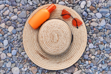 Fototapeta na wymiar Straw hat, bright red sunglasses and a bottle of sunscreen for sun protection