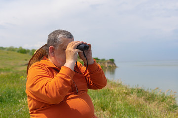 Outdoor portrait of senior man looking into binocular while sitting on Dnipro riverside at spring season