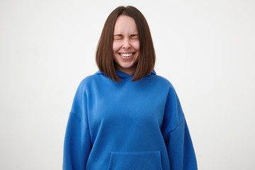 Good looking young pretty short haired brunette female dressed in blue hoodie smiling cheerfully...