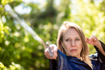 A female warrior with a sword poses on a stump in the forest. Wushu fencing