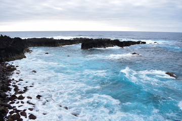 Sea water light splash on a sunset. Blue water along a rock shore.