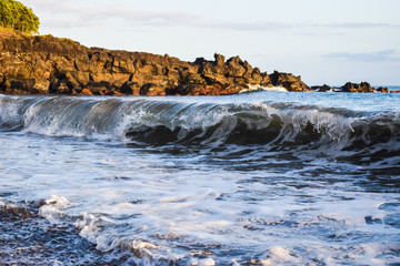 Sea water light splash on a sunset. Blue water along a rock shore.