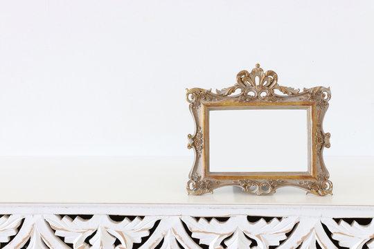Image of gold tone baroque vintage empty photo frame over wooden table. For mockup, can be used for photography montage