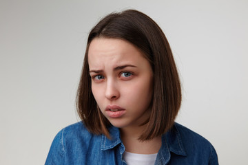 Close-up of young attractive short haired blue-eyed brunette lady squinting her eyes while looking wonderingly at camera, isolated over white background