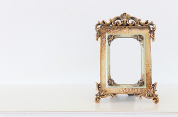 Image of gold tone baroque vintage empty photo frame over wooden table. For mockup, can be used for...