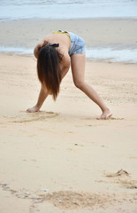 Fototapeta premium Summertime recreation concept. Young asian model in bikini preparing to flick hair posing action on sea beach. Woman in beachwear swimsuit stroll with on a sea coast.