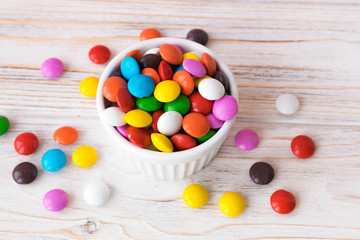 Colorful chocolate jelly beans in a white plate on a white wooden table