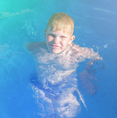 a strong blond boy with a smile swims in an outdoor pool. Child having fun in swimming pool. Summer vacation and healthy lifestyle concept