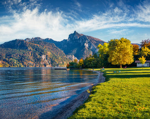 Colorful morning scene of Traunsee lake. Golden larch trees in the city park glowing last sunlight....