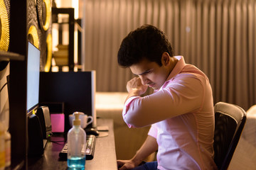 Young Indian businessman coughing on sleeve while working overtime at home during quarantine