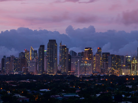 Makati, Metro Manila, Philippines - Afternoon Skyline with pink dramatic sky and city lights. View from Pasong Tamo extension. Wealthy low rise subdivision in front.