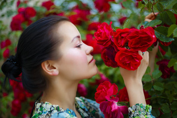 Fototapeta premium brunette woman smiling in a flowering bush of red roses