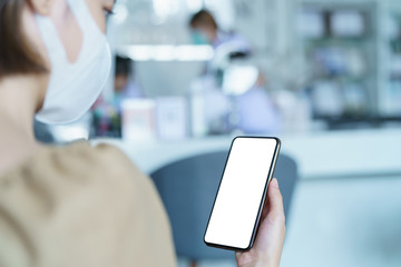 Woman wearing protective mask showing smart phone blank screen.