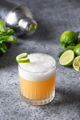 Pisco sour cocktail. Wiskey with lime, egg white, sugar syrup in glass on grey. Vertical. Close up.