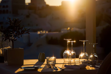 Restaurant table decorated with glasses on terrace in sunset light on the island Santorini, Cyclades, Greece