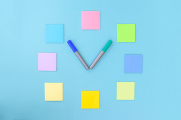 Clock made of colorful stickers and markers on blue background. Copy space, flat lay. Concept office and back to school.