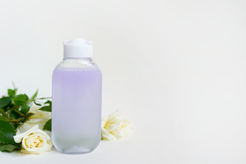 bottle with tonic or micellar cleansing water with flowers on light background, top view. Beauty, skin, hair or body care concept