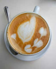 Top view of the white coffee cup with heart shape latte art foam on white table 