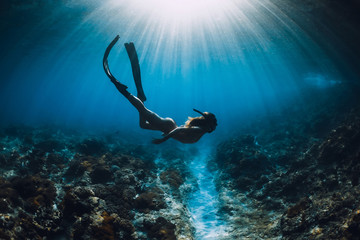 Young freediver woman with fins glides and amazing sun rays. Freediving underwater in ocean