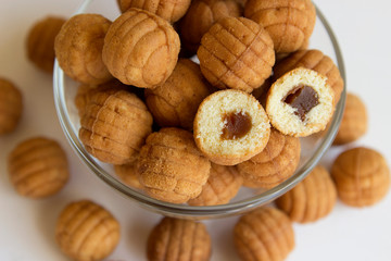 Round ruddy biscuit delicacy dessert in the form of small balls with boiled caramel inside. Cookies with filling are located in a transparent glass bowl and are scattered nearby on a white table.