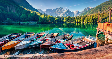 Six pleasure boats on Fusine lake. Calm morning view of Julian Alps with Mangart peak on...
