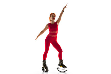 Fototapeta na wymiar Beautiful redhead woman in a red sportswear jumping in a kangoo jumps shoes isolated on white studio background. Jumping high, active movement, action, fitness and wellness. Fit female model.
