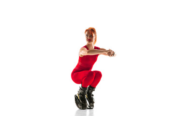 Beautiful redhead woman in a red sportswear jumping in a kangoo jumps shoes isolated on white studio background. Jumping high, active movement, action, fitness and wellness. Fit female model.
