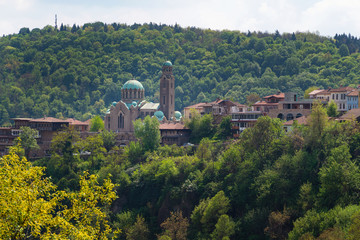 St Demetrius orthodox cathedral in Veliko Tarnovo city, Bulgaria. Tourist attraction surrounded by trees and mountain.