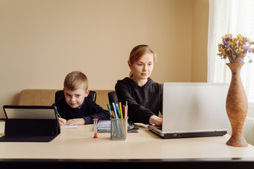 Mother using laptop and tablet teaching with her son online at home in his room