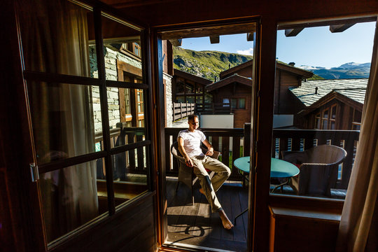 A young man in the morning looks from the hotel balcony with a view of the mountains. Mountain views at the hotel resort - Powered by Adobe