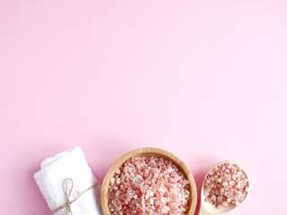 Spa flatlay composition. Sea salt in wooden jar and in spoon, bath towel on pink background. Copyspace, top view. Home care concept, relax and rest, bath procedure