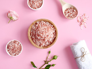 Fototapeta na wymiar Spa flatlay composition. Sea salt in wooden jar and scattered from spoon, towel, flower on pink background. Top view. Daily care concept, relax and rest, bath procedure