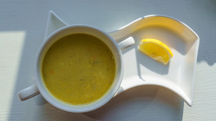 Top view of a plate with lentil soup and lemon stand on a white wooden table in the rays of lighting.