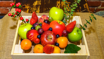 Set of berries and fruits in wooden box. Apple, strawberry, grape, berry and peach on a red brick...