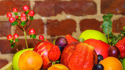 Set of berries and fruits in wooden box. Apple, strawberry, grape, berry and peach on a red brick background.