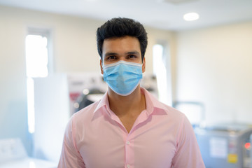 Young Indian businessman wearing mask while doing laundry indoors