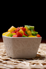 Vegetables in white bowls, diced on a brown kitchen table. Peppers, cucumbers, sweet corn and peas in a bowl on the table.