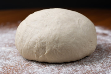 Fototapeta na wymiar A kneaded dough with flour and water for homemade bread lying on a brown table with a black background.