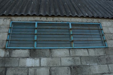 Fototapeta na wymiar one blue old metal window with iron bars on the gray brick wall of the attic under a slate roof