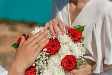 Hands of the groom and the bride with wedding rings on top of the bride's bouquet