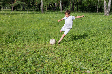 9 years old boy beats his leg soccer ballin white uniform playing football in green summer park