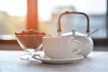  White coffee cup with roasted coffee beans and morning sunrise at the windows background