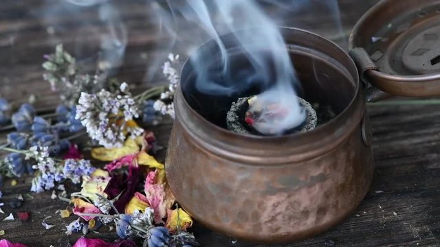 Weihrauchmischung verbrennt blubbernd und rauchend auf einer Räucherkohle in einem Räuchergefäß aus Kupfer dekoriert mit getrockneten Kräutern und Blüten-Räucherritual