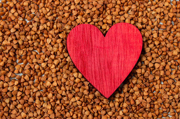 red heart made of wood on a background of buckwheat. Gluten-free and healthy diet. I love buckwheat concept.