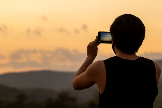 Silhouette of man taking photos of sunset with mobile phone in twilight time. Modern lifestyle