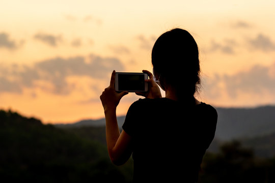 Silhouette of women taking photos of sunset with mobile phone in twilight time. Modern lifestyle