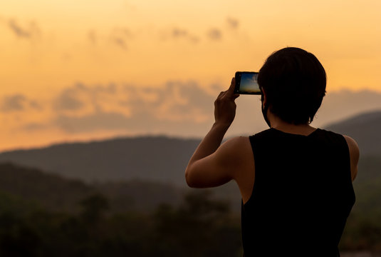 Silhouette of man taking photos of sunset with mobile phone in twilight time. Modern lifestyle