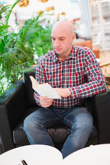 a man in a shirt sits in a chair in an apartment reading a book