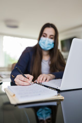 Young woman wearing medical face mask working from home. Freelancer or online learning concept during coronavirus pandemic.