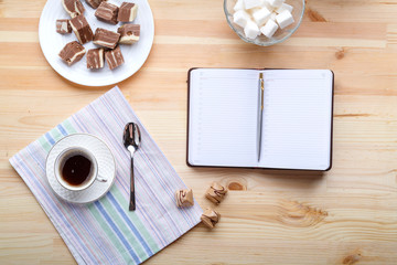Cup of coffee on a wooden table with sweets and notepad.